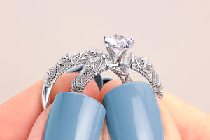 Silver ring with a large diamond held between fingers with light blue nail polish on a neutral background