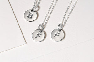 Three silver necklaces with round pendants engraved with initials on a light background.